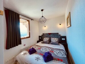 A bedroom with a bed, a window with curtains, a wall-mounted light, and a ceiling light fixture. - Apprt Front de Neige Aussois -6 Pers- Le Marmotton (Aussois)