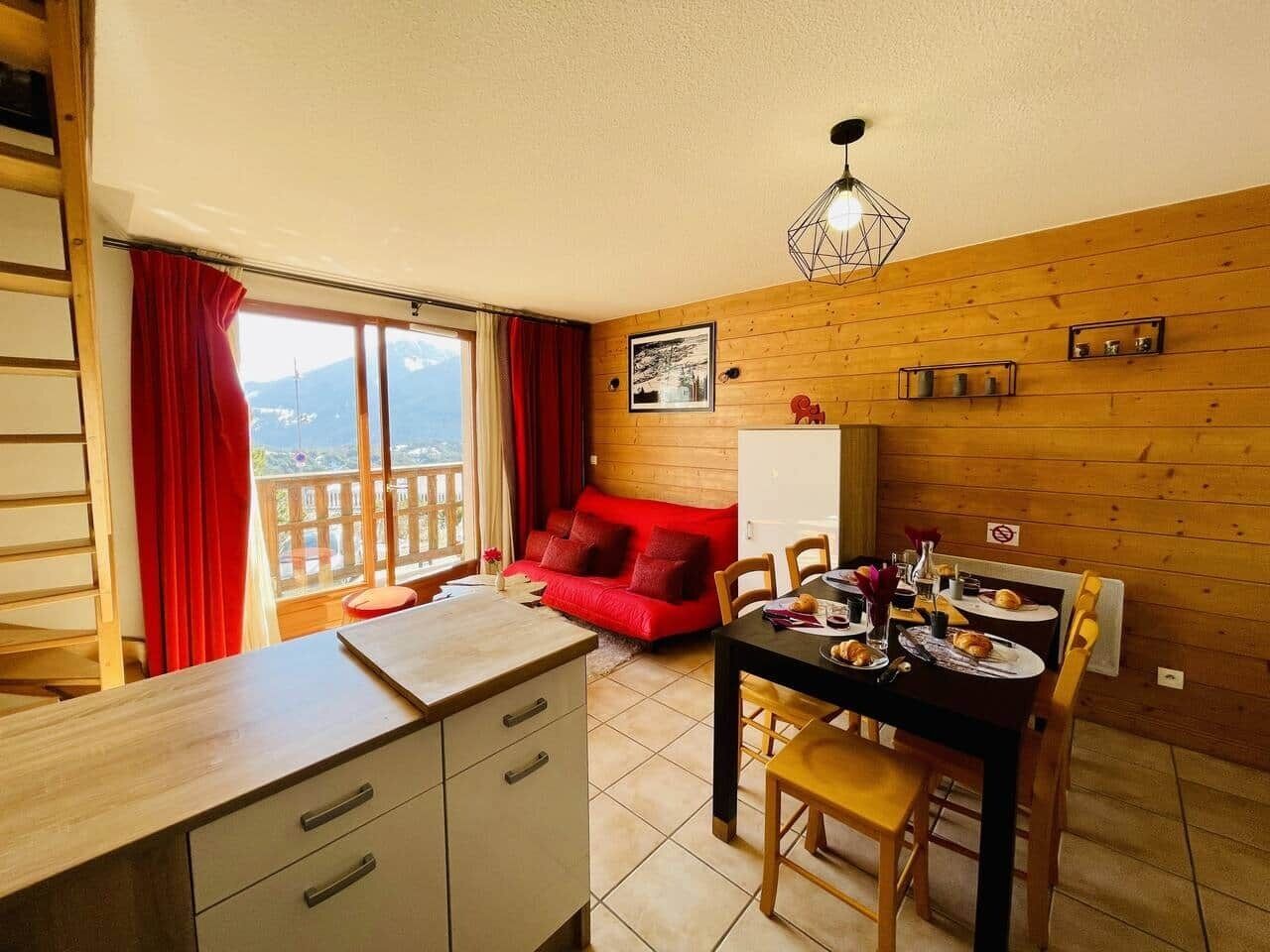 A cozy room with a dining table set for two, a red sofa, and a view of the outdoors.