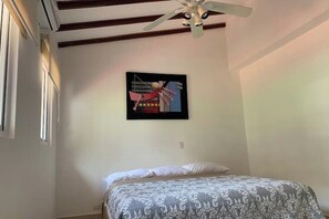 Ein Schlafzimmer mit einem Bett, einem Deckenventilator, einem gerahmten abstrakten Gemälde und einem Fenster.