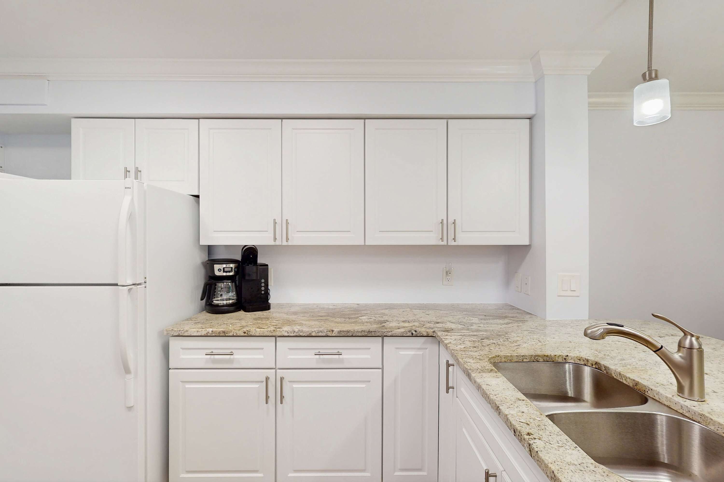 A kitchen with white cabinets, a granite countertop, a stainless steel sink, and a coffee maker.