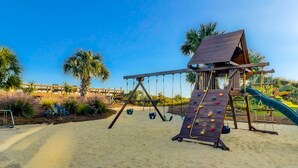 Un parque infantil en la playa con pared de escalar, columpios y tobogán.