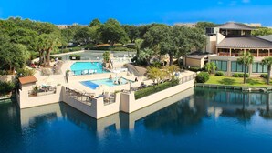 Un resort con varias piscinas, un edificio grande con techo plano y exuberante vegetación que lo rodea.