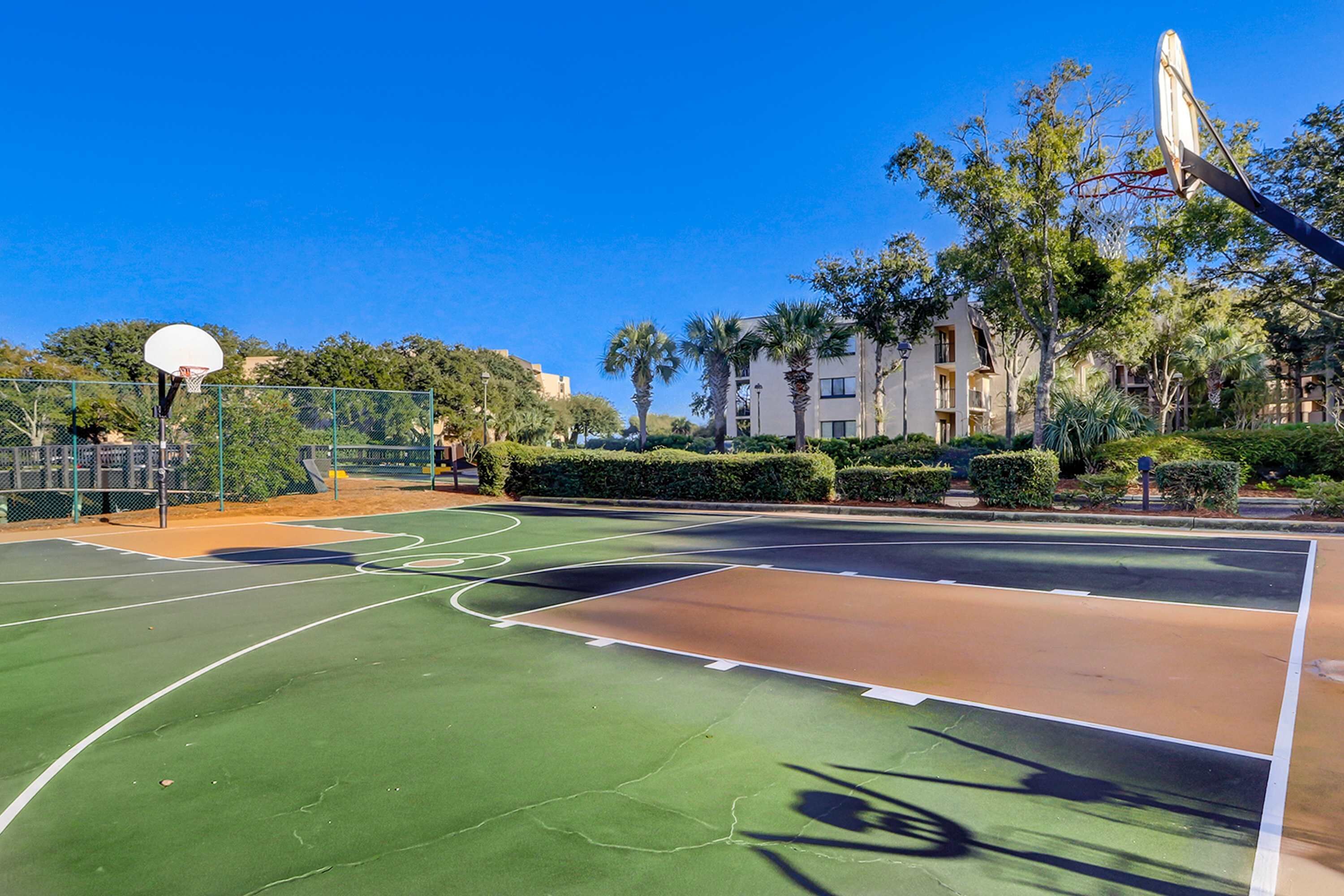 Ein Basketballplatz im Freien mit Korb, umgeben von Grünflächen und Gebäuden.
