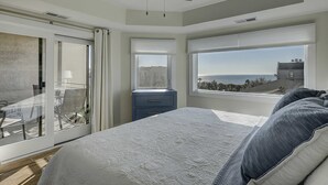A bedroom with a bed, a nightstand, a dresser, a ceiling fan, and a large window with a view of the sea. - Beautiful condo with ocean & pool views, hot tub and snowbird friendly (Hilton Head)