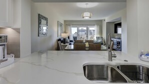 A modern kitchen with a marble countertop, stainless steel sink, and a dining area with wicker chairs and a table. - Beautiful condo with ocean & pool views, hot tub and snowbird friendly (Hilton Head)