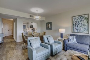 Ein Wohnzimmer mit zwei Sofas, einem Essbereich mit Tisch und Stühlen, einer Küche im Hintergrund und einem Gemälde an der Wand.