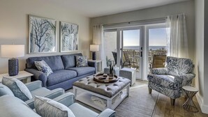 A living room with a sofa, armchairs, a coffee table, and artwork on the walls. - Beautiful condo with ocean & pool views, hot tub and snowbird friendly (Hilton Head)