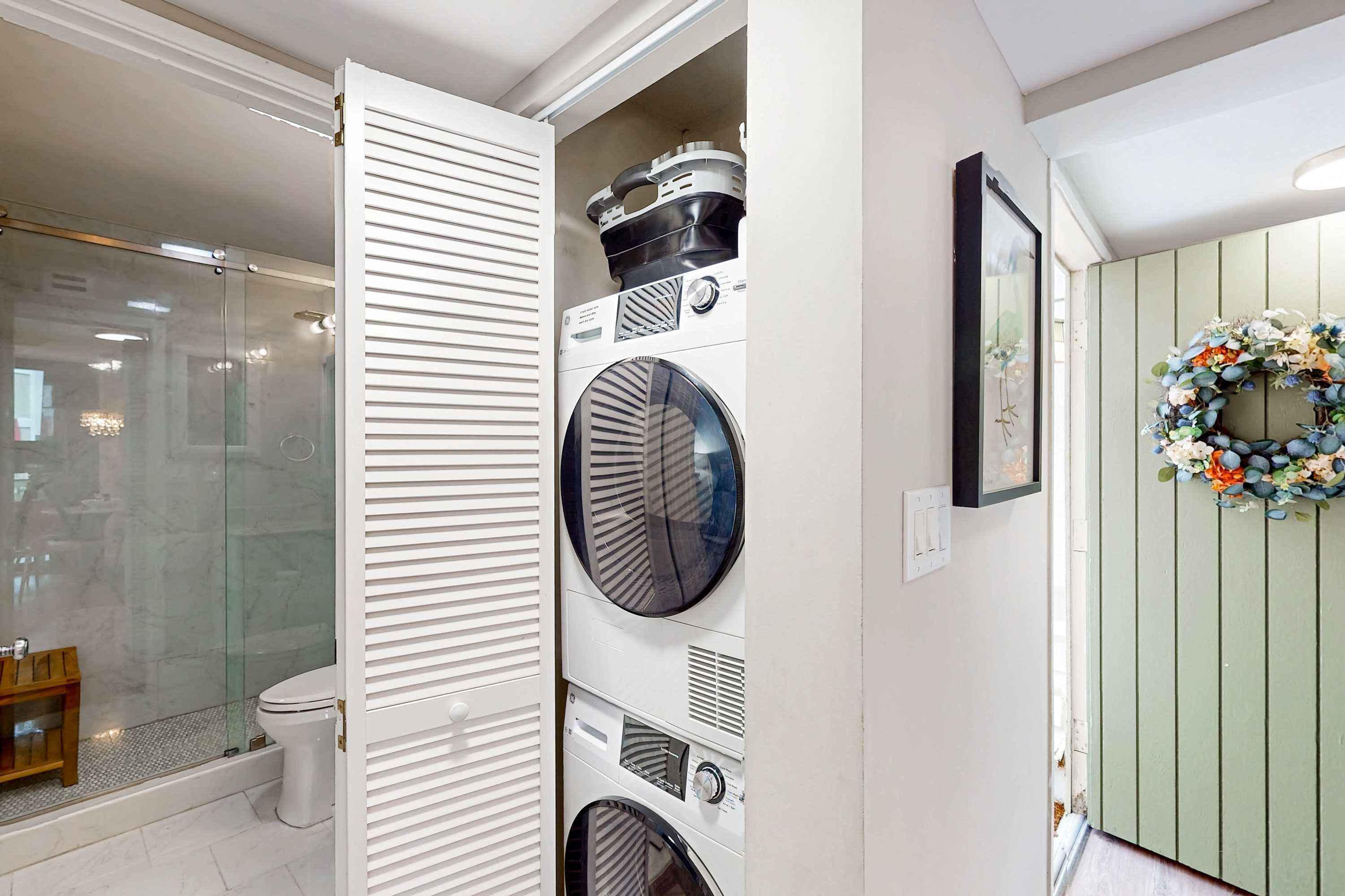 A laundry area with stacked washing machines, a glass shower enclosure, and a green wall with a floral wreath.