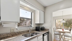 A kitchen with a granite countertop, white cabinets, a built-in dishwasher, a window with a view, and a dining area with a table and chairs. - Spacious lagoon-view condo with tennis, outdoor pool, beach access, balcony (Hilton Head)