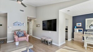 A living room with a ceiling fan, a TV, a pink chair, a coffee table, and a patterned rug. - Spacious lagoon-view condo with tennis, outdoor pool, beach access, balcony (Hilton Head)