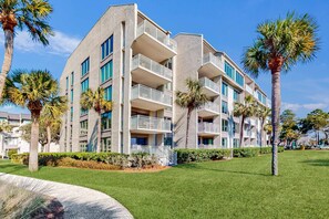A multi-story hotel with balconies, palm trees, and a well-maintained lawn. - First Floor Condo near the beach with beach gear, washer and dryer, and pool (Hilton Head)