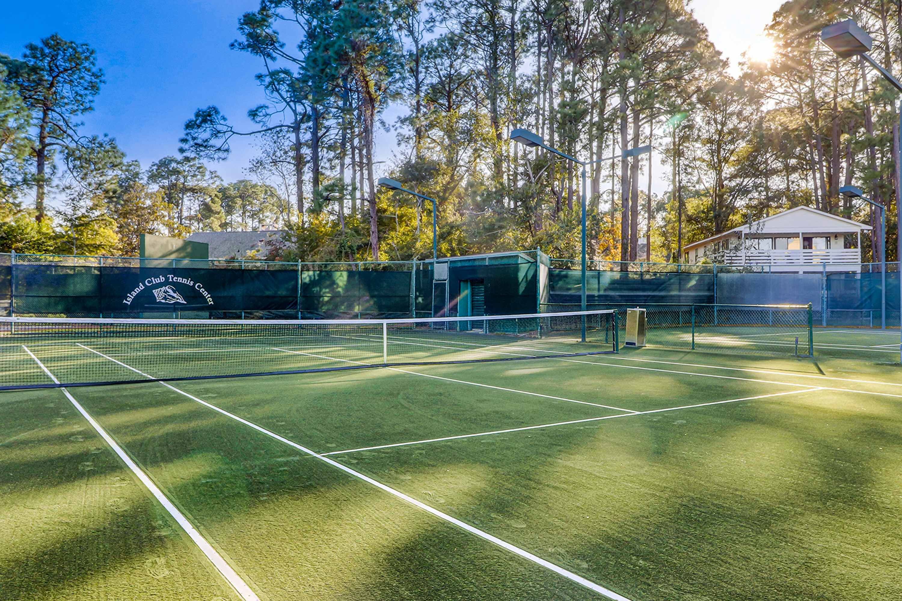 Een tennisbaan met een net, omringd door bomen en een gebouw op de achtergrond.