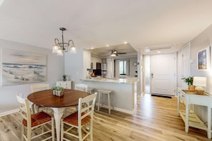 A dining area with a wooden table and chairs, a kitchen with a central island, and a ceiling fan. - Bright condo with shared pools/hot tub and tennis court,  walk to beach (Hilton Head)