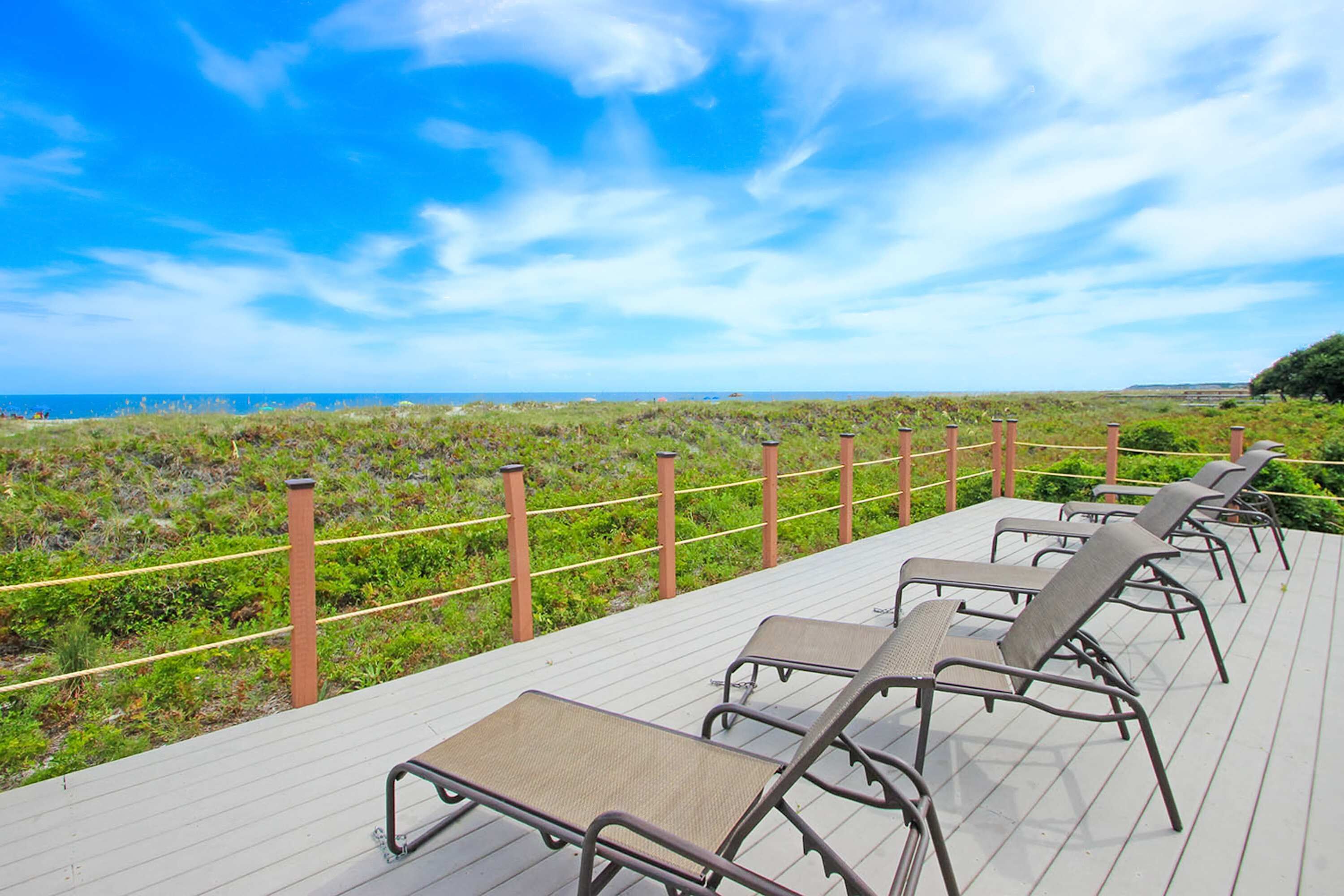 A deck with lounge chairs overlooking a beach.