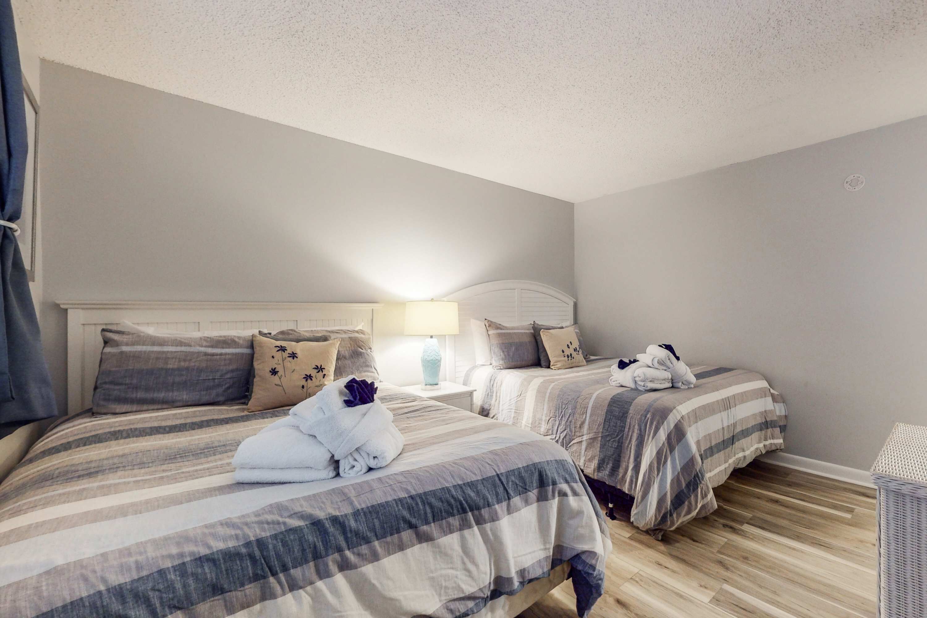 A hotel room with two beds, a nightstand with a lamp, and a small table.