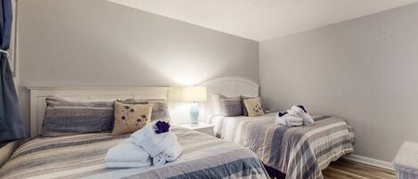 A hotel room with two beds, a nightstand with a lamp, and a small table.