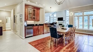 Una cocina moderna con armarios de madera, un comedor con mesa y sillas de madera, y ventanas grandes que ofrecen luz natural.