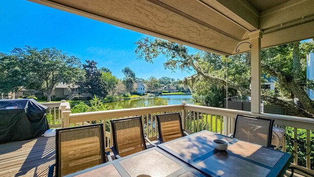 Un patio al aire libre con mesa y sillas, con vista a un lago y follaje.