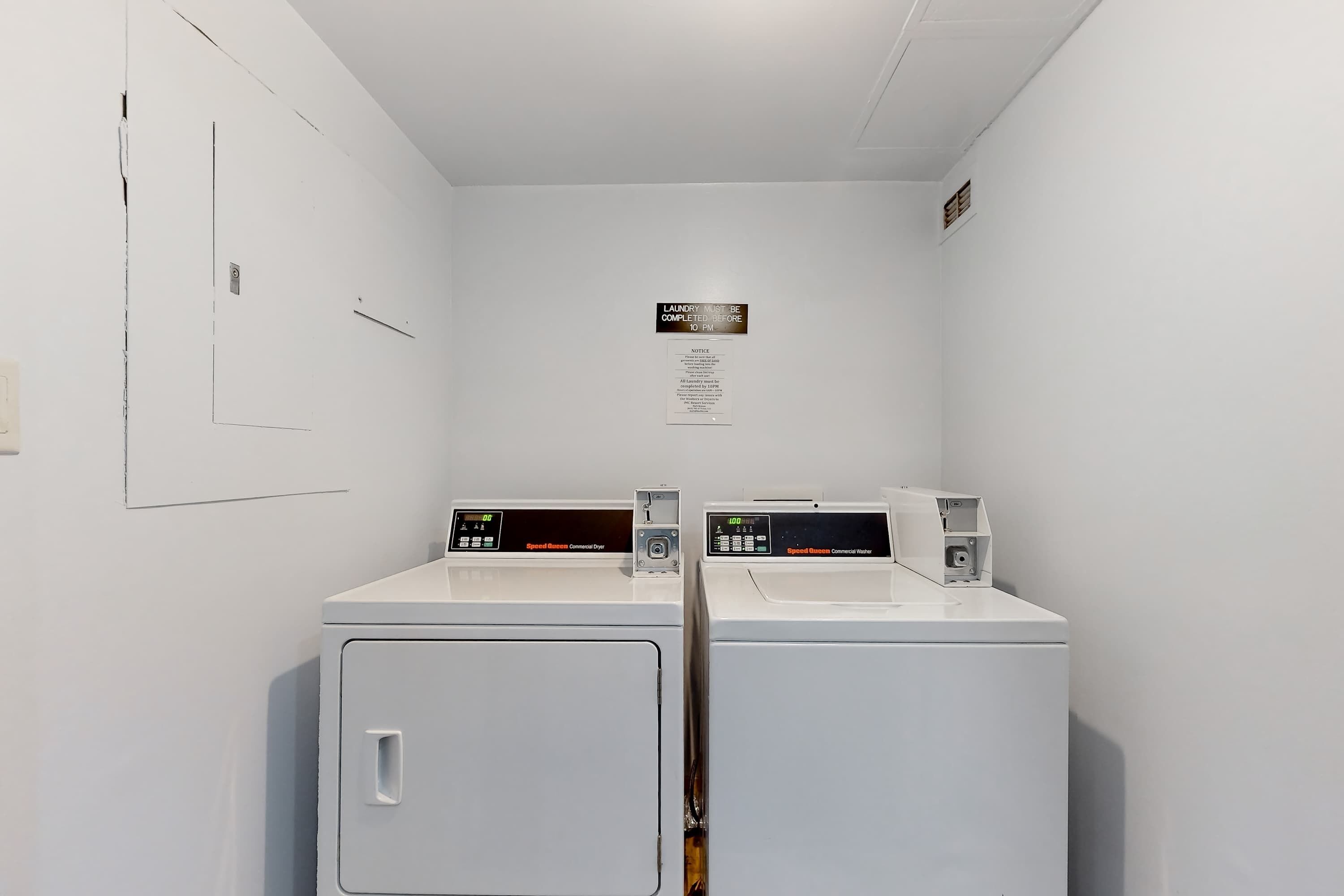 A laundry room with two front-loading washers and dryers, a notice on the wall, and a door with a handle.