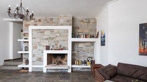 Een woonkamer met een stenen open haard, witte planken, een bruine bank en een kroonluchter.