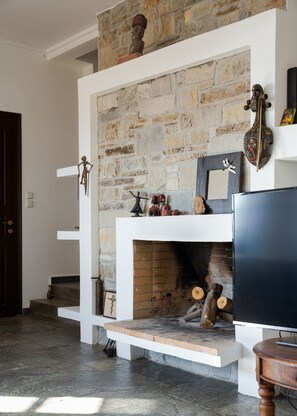 A stone fireplace with a TV on a stand, a wooden door, and a staircase. - My Way Kavos Villa, Bill & John Aegina (Aegina)