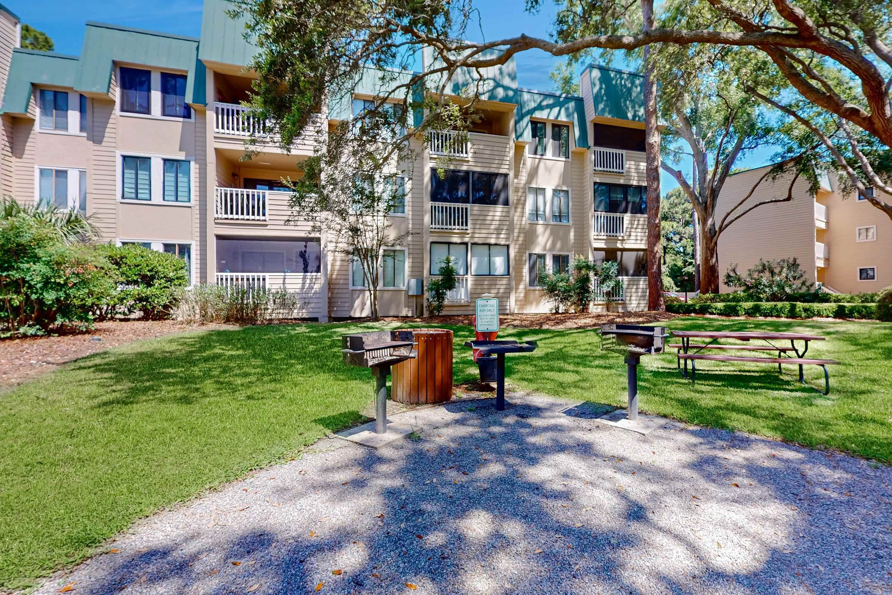 Un immeuble résidentiel à plusieurs étages, doté de balcons, d’un espace barbecue et d’une table de pique-nique, le tout situé dans une pelouse bien entretenue.