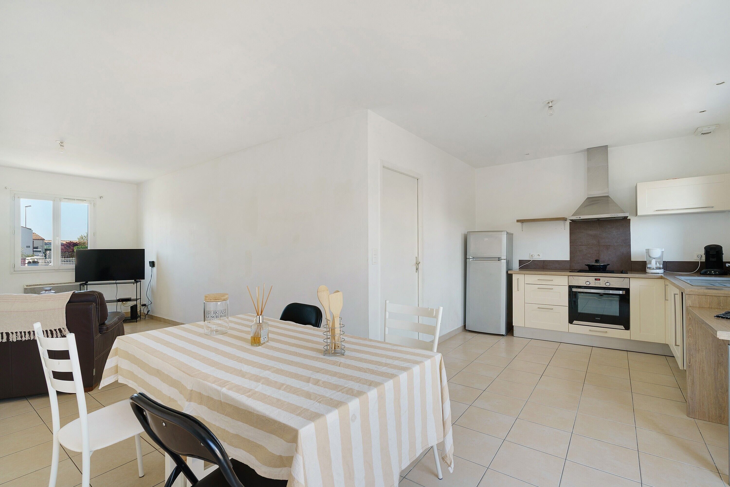 A modern kitchen with a stove, oven, and microwave. There is a dining area with a striped table and chairs.