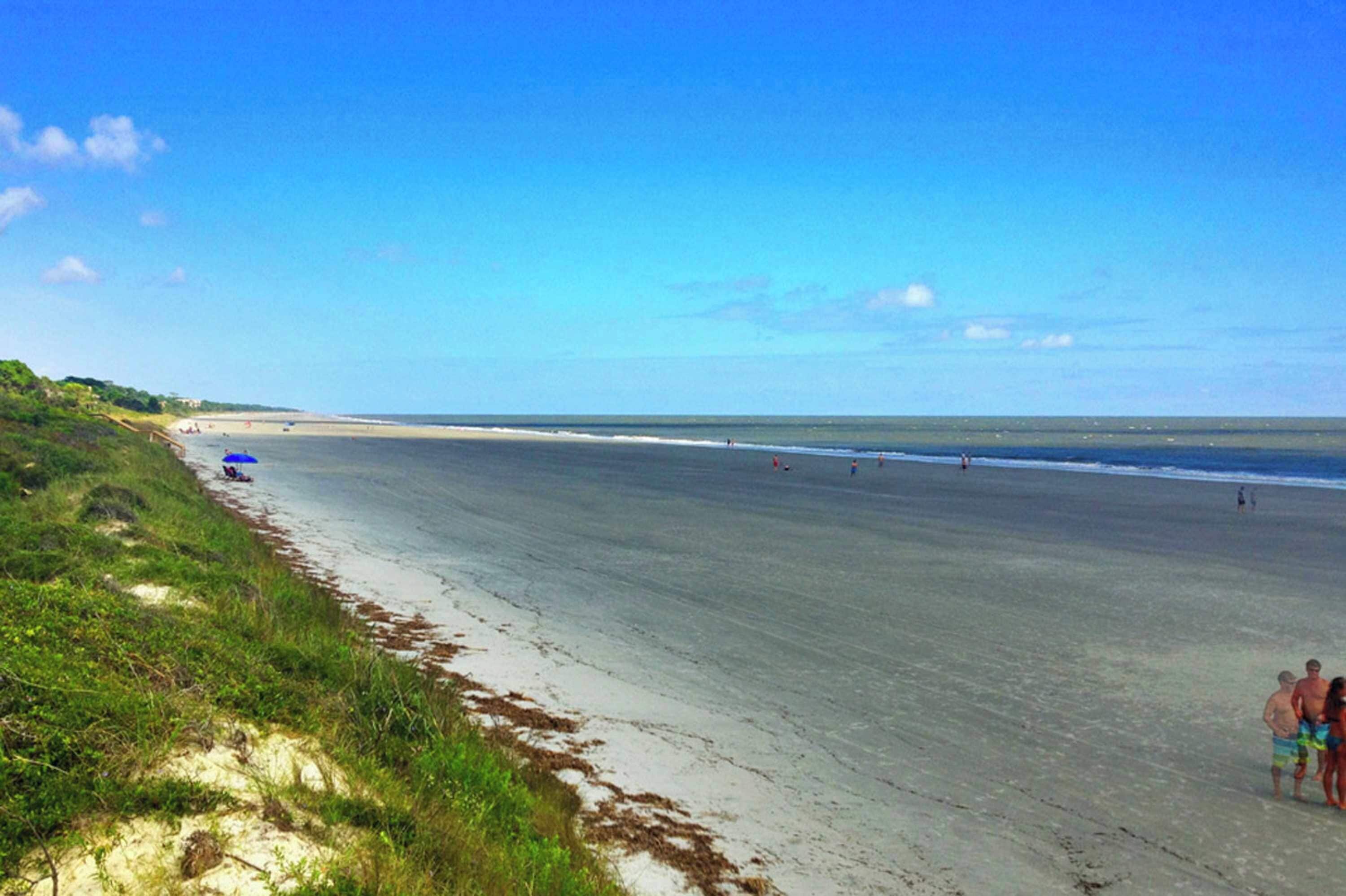A beach with a sandy shore, a few people, and a clear sky.