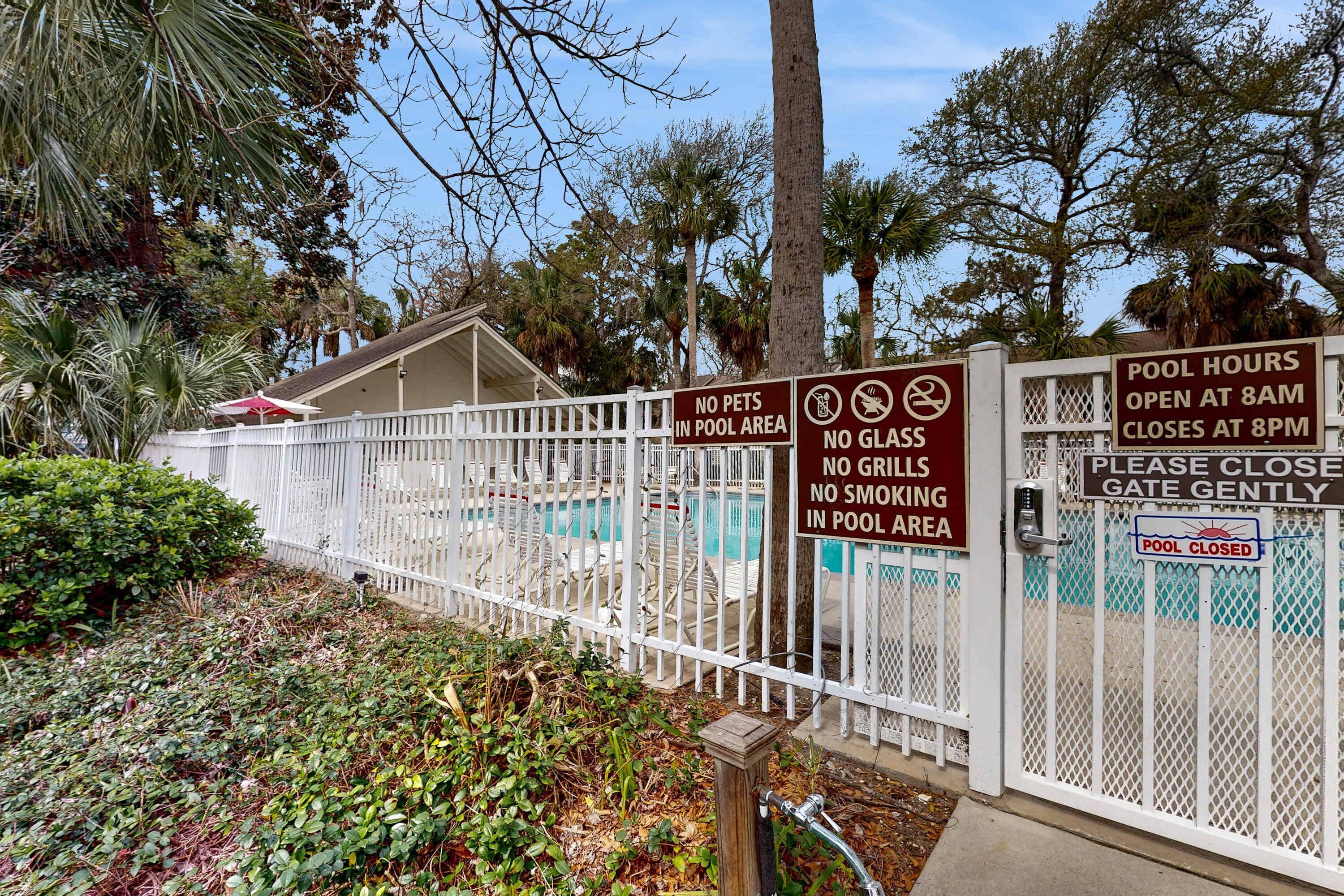 A gated pool area with signs indicating no pets, no glass, no grills, no smoking, and pool hours from 8 AM to 8 PM.