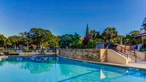 Piscina com parede de pedra, escadaria e vista para árvores e um edifício ao fundo.