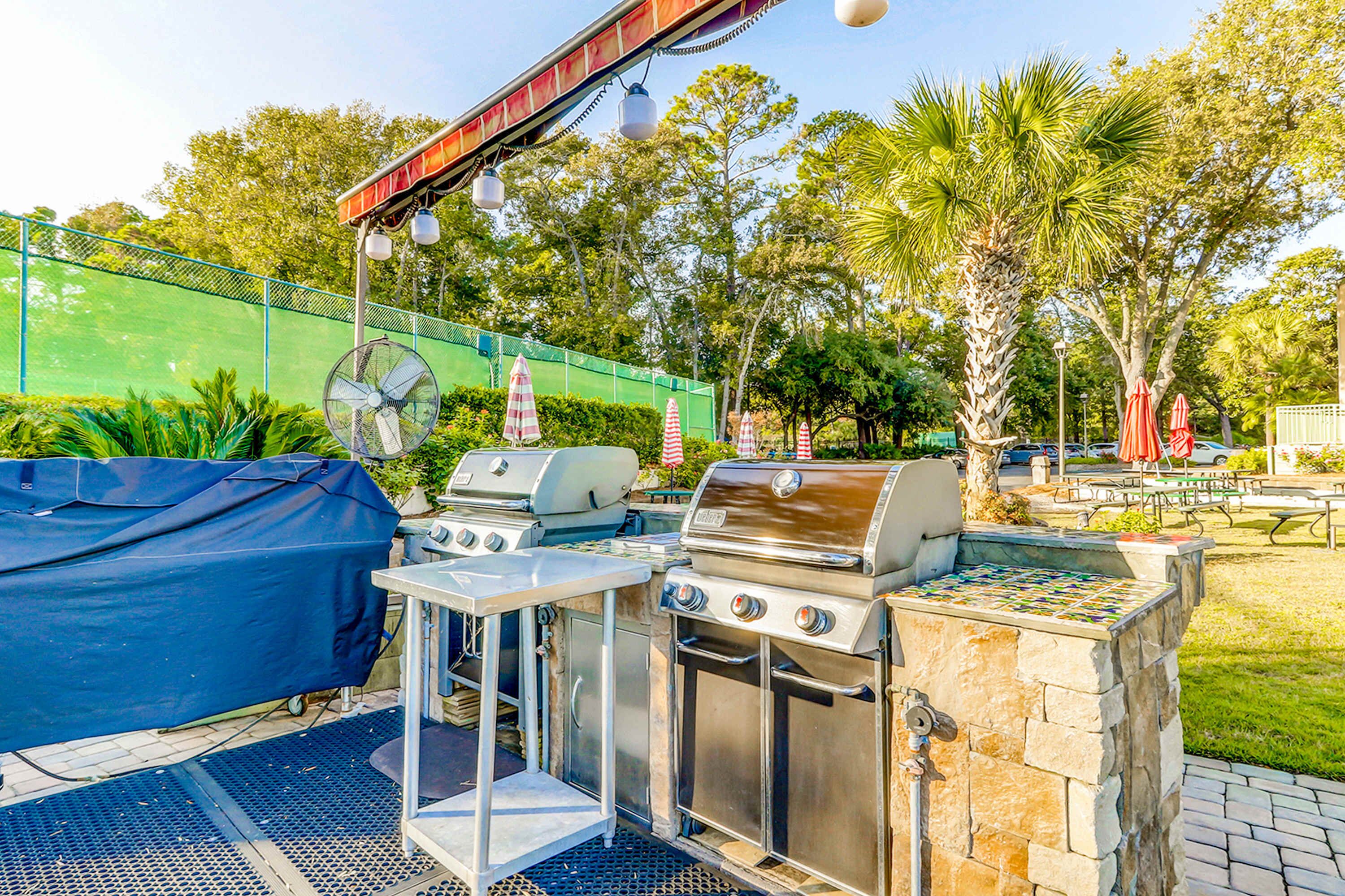 Een buitenbarbecueplaats met een overdekte grill, een ventilator en een grillstation van steen.