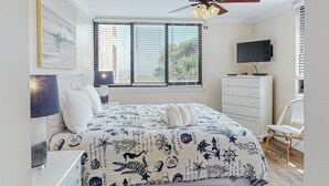 Quarto com cama, televisão, penteadeira, cadeira e ventilador de teto.