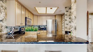 Una cocina con una isla central, electrodomésticos de acero inoxidable y papel tapiz estampado.