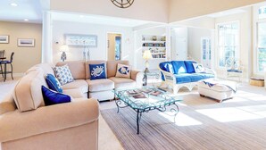 A spacious living room with a beige sectional sofa, a glass coffee table, and a blue accent sofa. - Spacious Home with Private Pool, Game Room, & Big Backyard - Great for Groups (Hilton Head)