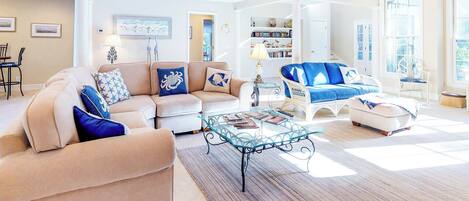 A spacious living room with a beige sectional sofa, a glass coffee table, and a blue accent sofa.