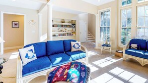 A spacious living room with a blue sofa, a patterned rug, and a bookshelf filled with books. - Spacious Home with Private Pool, Game Room, & Big Backyard - Great for Groups (Hilton Head)