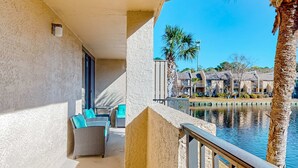 A balcony with a view of a water body, palm trees, and a building complex in the background. - Updated Condo with Lagoon Views, Shared Pool, Hot Tub & WiFI - Near Beach (Hilton Head)