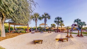 A sandy outdoor area with wooden benches, a gazebo, palm trees, and a playground. - Updated Condo with Lagoon Views, Shared Pool, Hot Tub & WiFI - Near Beach (Hilton Head)