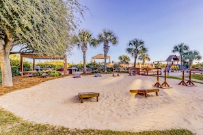 A sandy outdoor area with wooden benches, a gazebo, palm trees, and a playground. - Updated Condo with Lagoon Views, Shared Pool, Hot Tub & WiFI - Near Beach (Hilton Head)