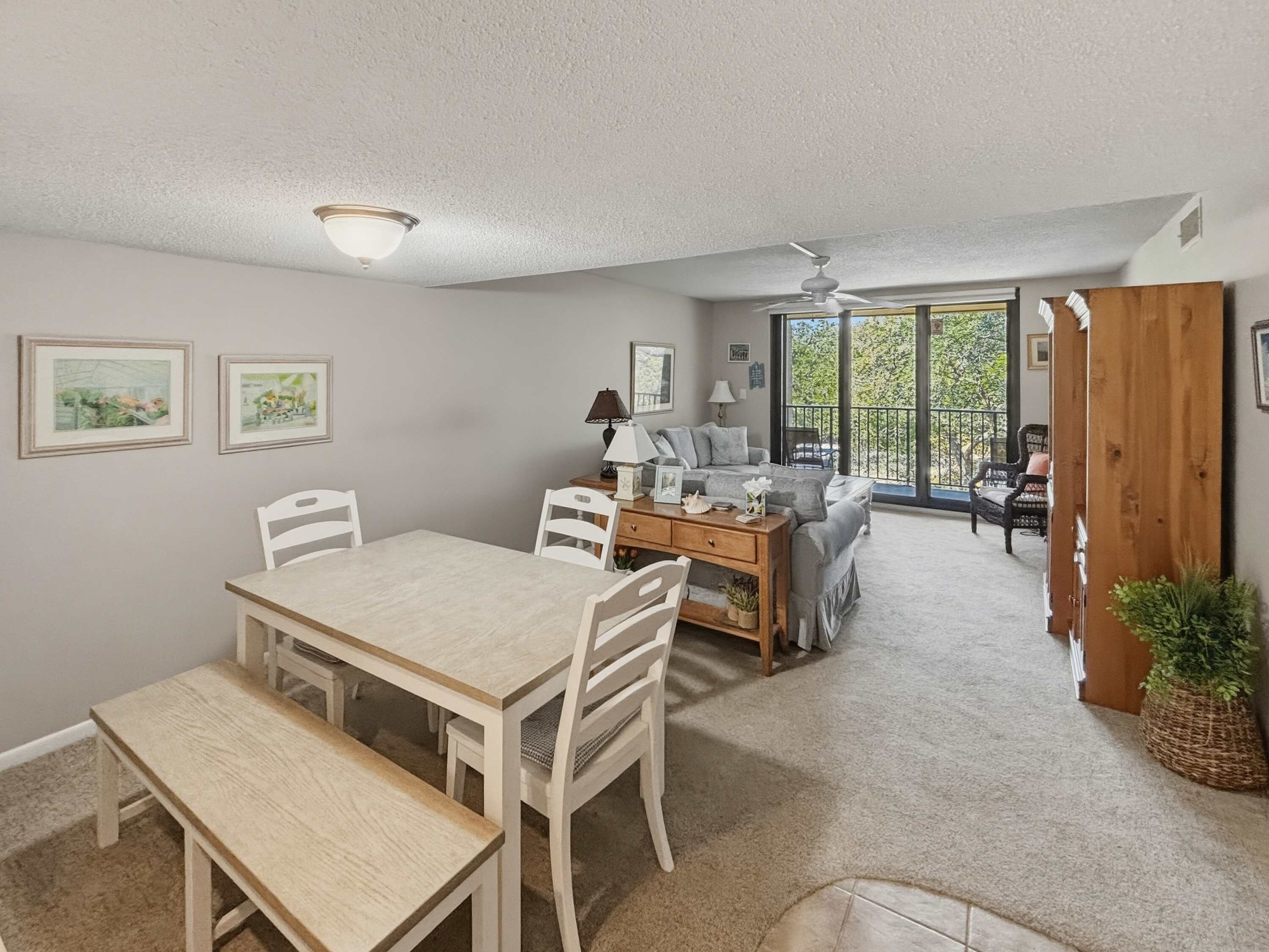 A spacious living area with a dining table, chairs, a sofa, and a balcony with a view.