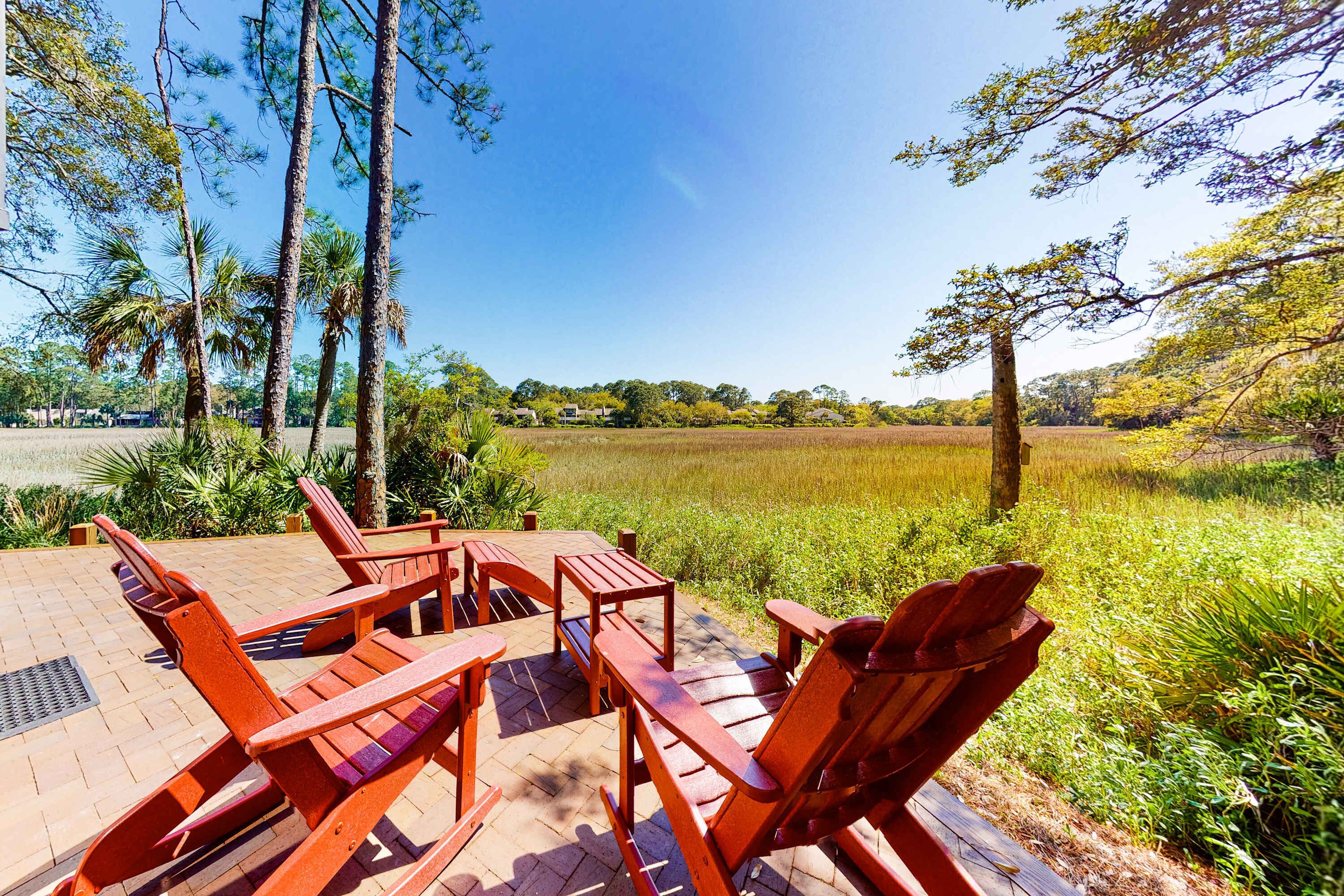 Une terrasse avec des chaises et des tables en bois, donnant sur un champ et des arbres.