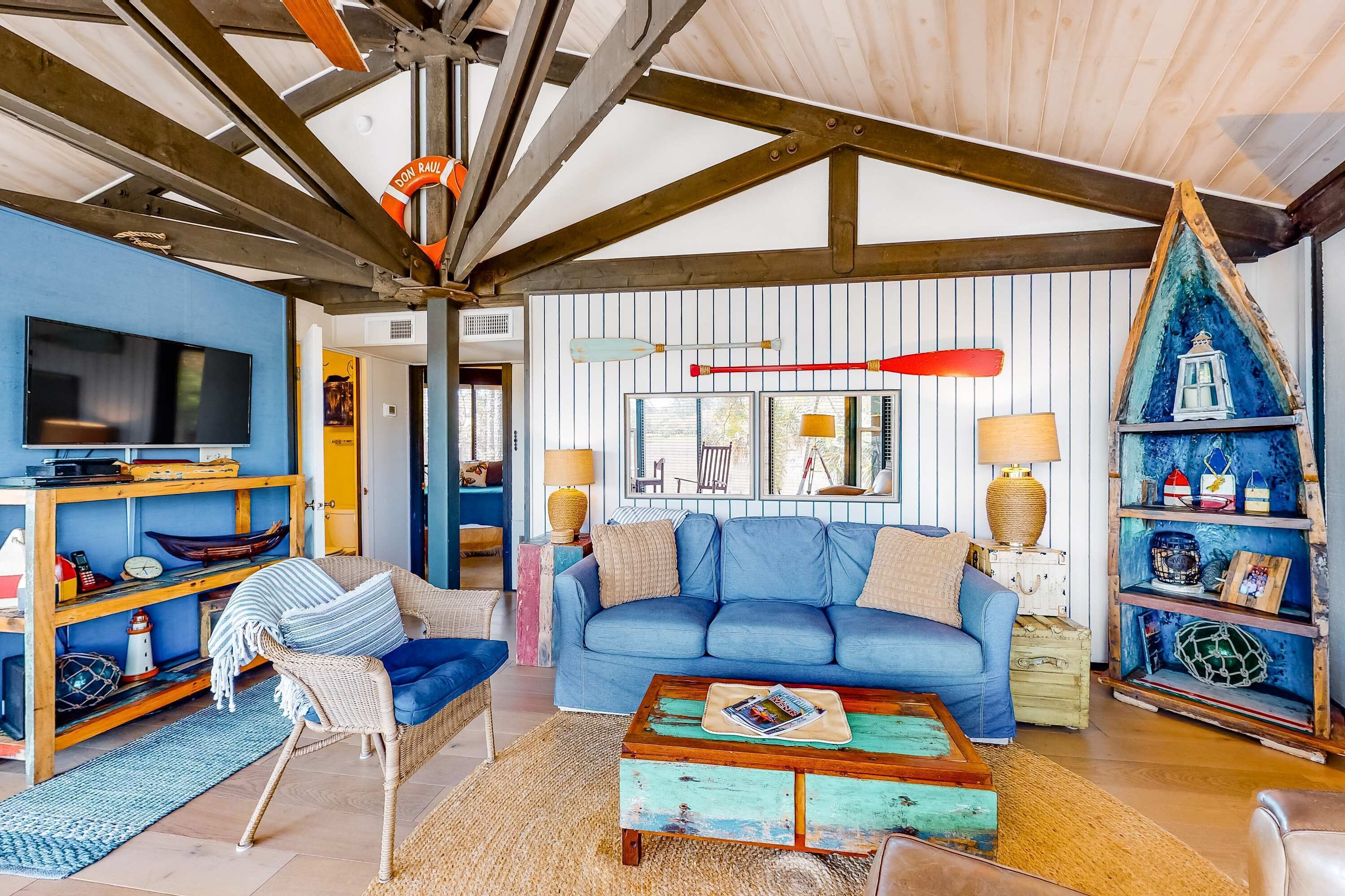 Una sala de estar con un sofá azul, una mesa de centro de madera y una estantería con detalles náuticos.