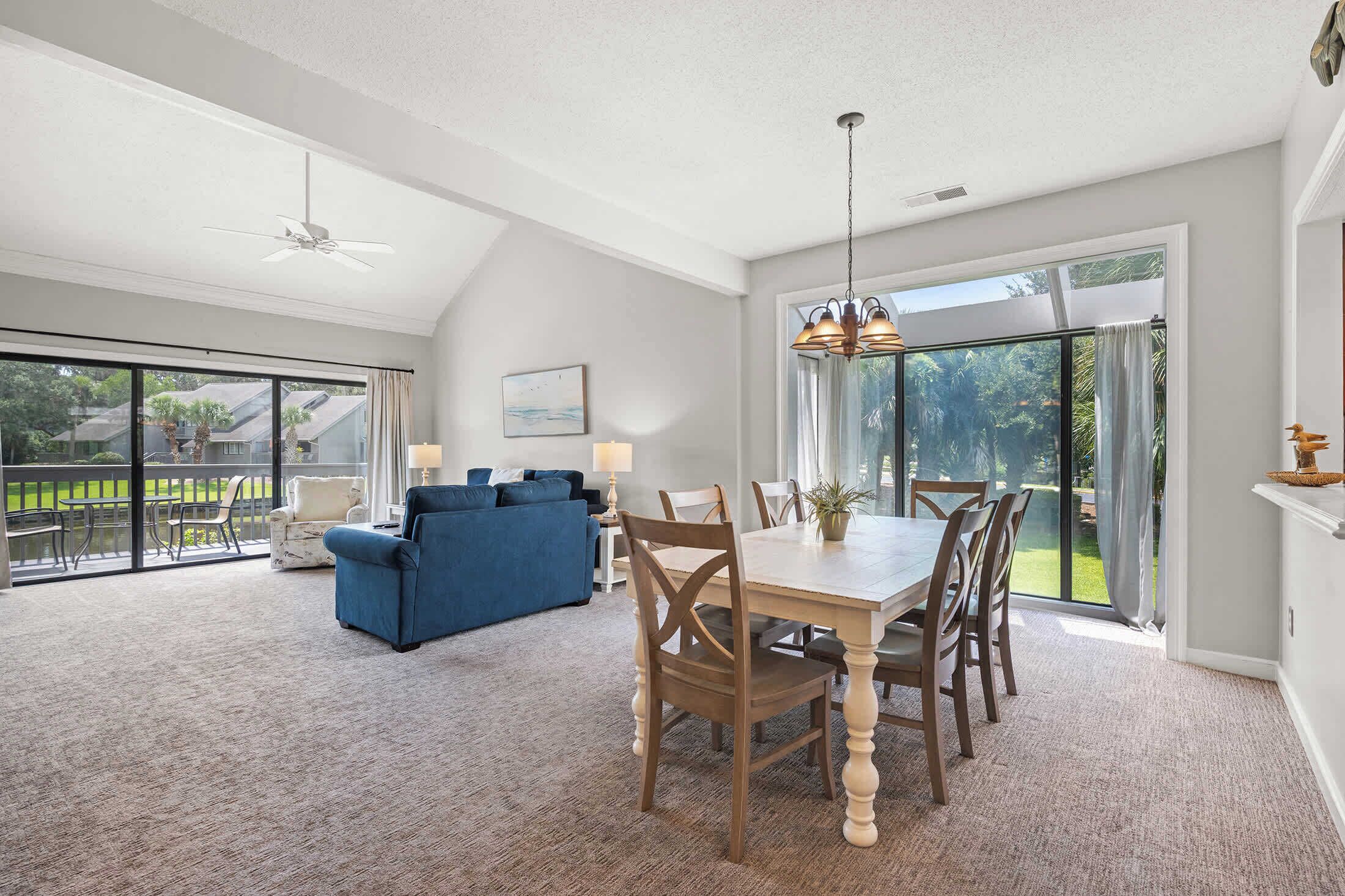 A spacious living area with a dining table, blue sofa, and a view of a garden through large sliding doors.