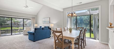 A spacious living area with a dining table, blue sofa, and a view of a garden through large sliding doors.