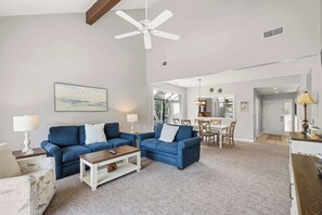 Ein Wohnzimmer mit blauem Sofa, einem Couchtisch und einem Essbereich mit Tisch und Stühlen.