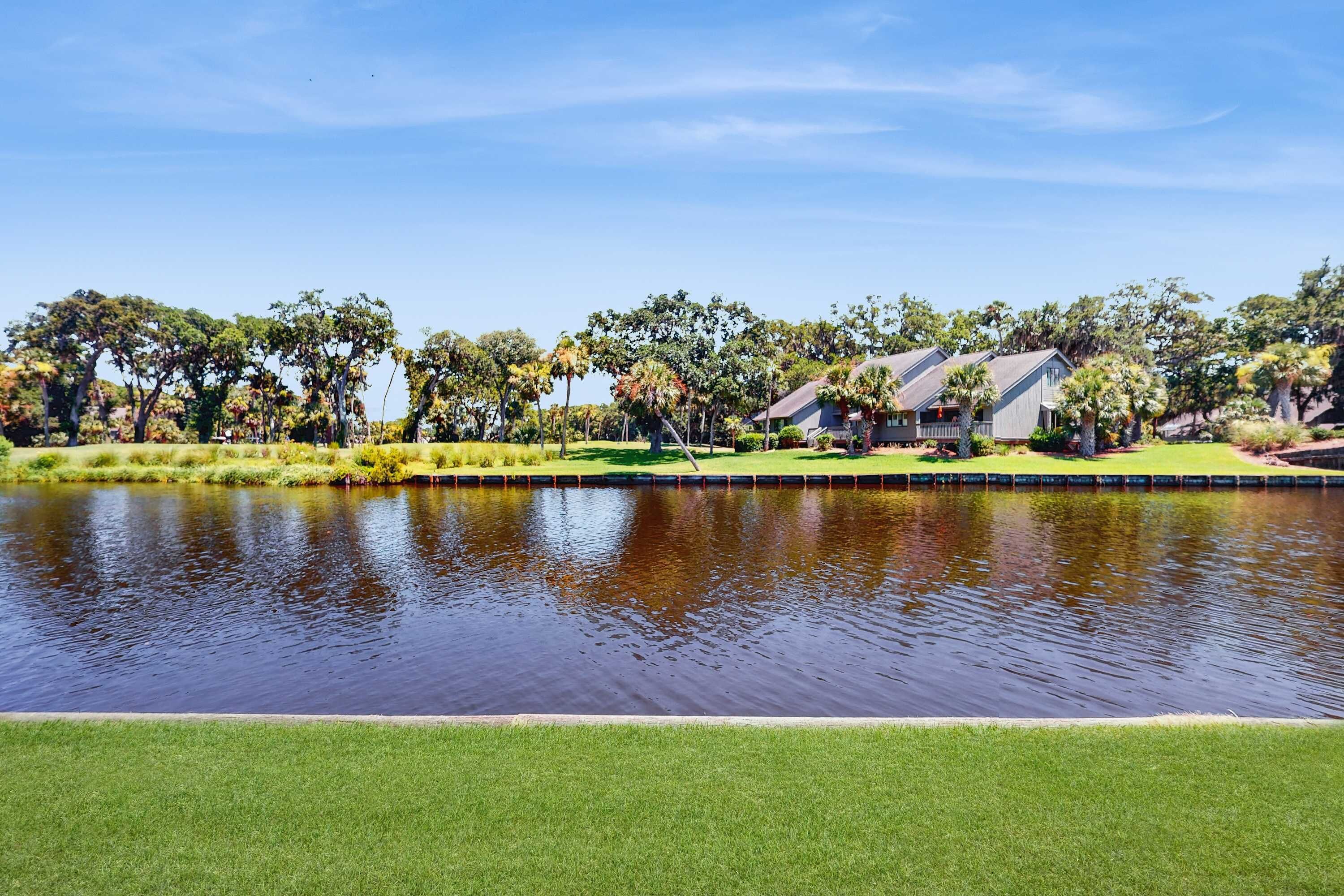 A serene lakeside view with a well-maintained lawn, a small dock, and a row of houses with a consistent architectural style.