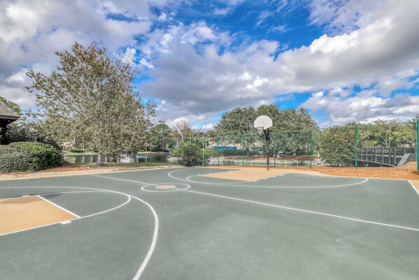 An outdoor basketball court with a hoop, surrounded by trees and a fence. - Oceanfront Condo with Shared Pool, Hot Tub, Beach Access & Playground (Hilton Head)