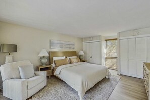 A bedroom with a bed, a chair, a nightstand, a lamp, a dresser, a closet, and a window with blinds. - Lagoon front, 3 story condo w balcony & washer dryer, snowbird-friendly (Hilton Head)