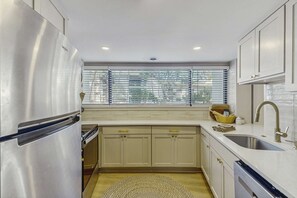 A modern kitchen with stainless steel appliances, beige cabinetry, a window with blinds, and a built-in dishwasher. - Lagoon front, 3 story condo w balcony & washer dryer, snowbird-friendly (Hilton Head)