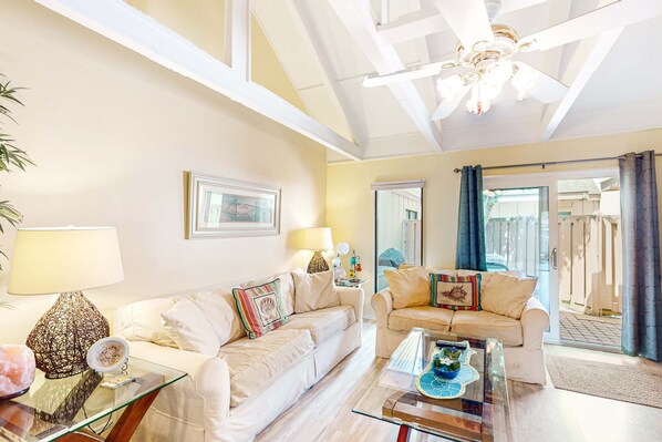 A spacious living room with two white sofas, a glass coffee table, and a ceiling fan. - Lovely villa near the water with private fenced courtyard,shared pools, tennis courts (Hilton Head)